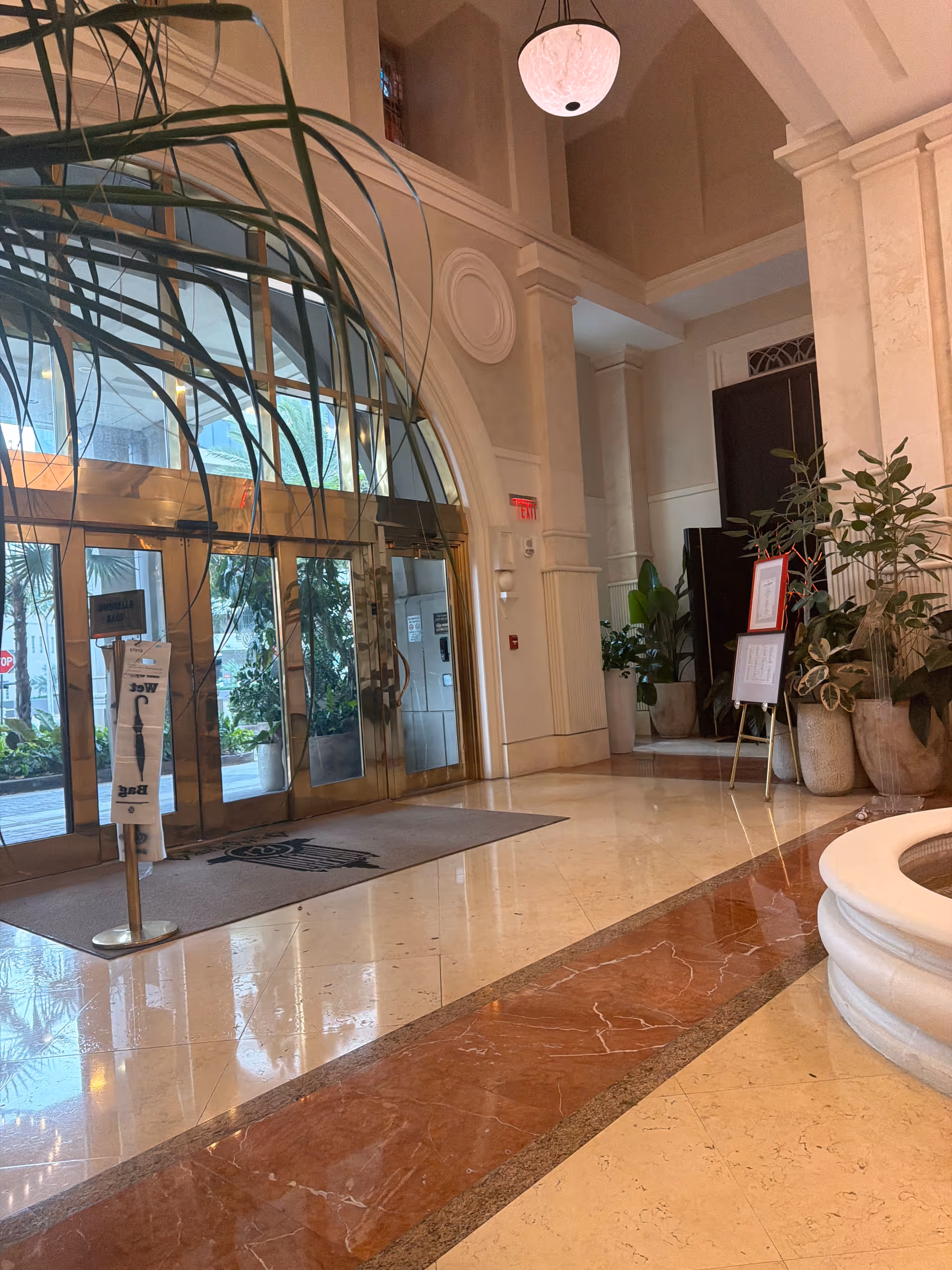 Luxurious hotel-like lobby with glass doors, marble floors, and tall potted plants.