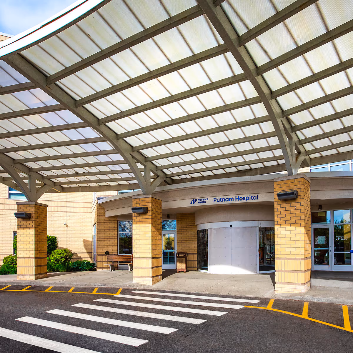 Hospital entrance beneath curved glass canopy with brick pillars at Putnam Hospital.