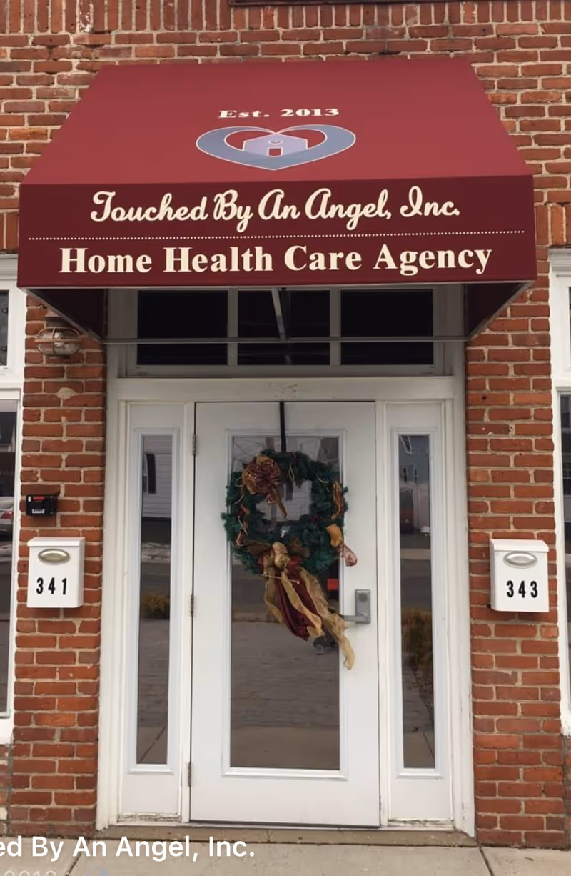 Brick building entrance with maroon awning signage reading Touched By An Angel Home Health Care Agency.