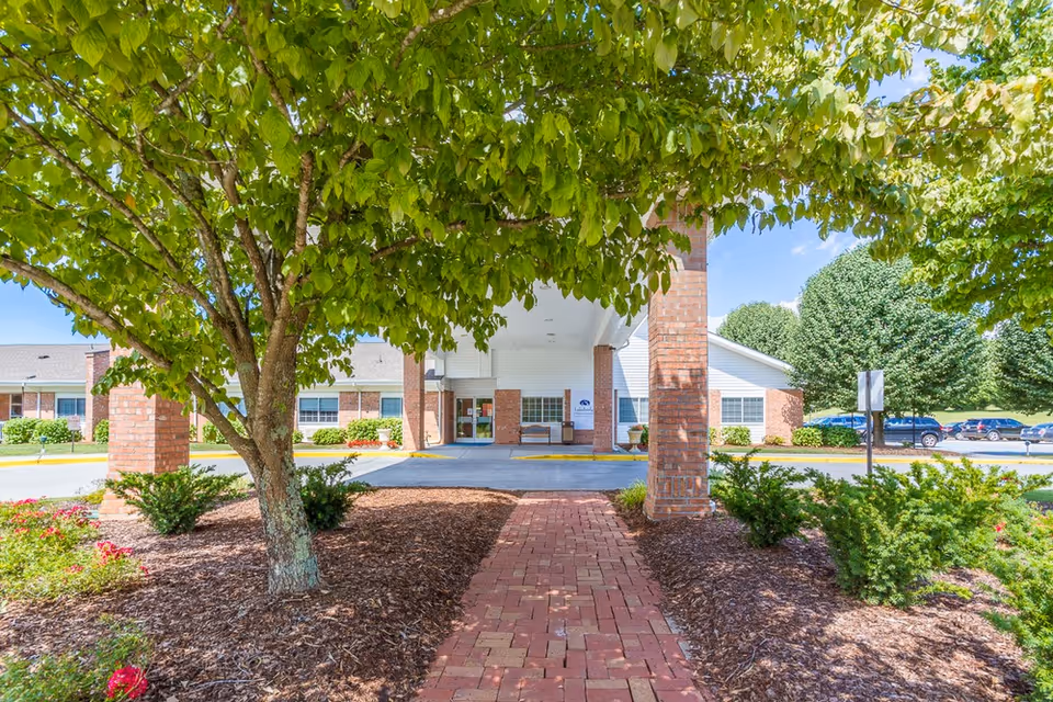 Brick walkway to a covered entrance of Lakebridge, surrounded by trees and shrubs.