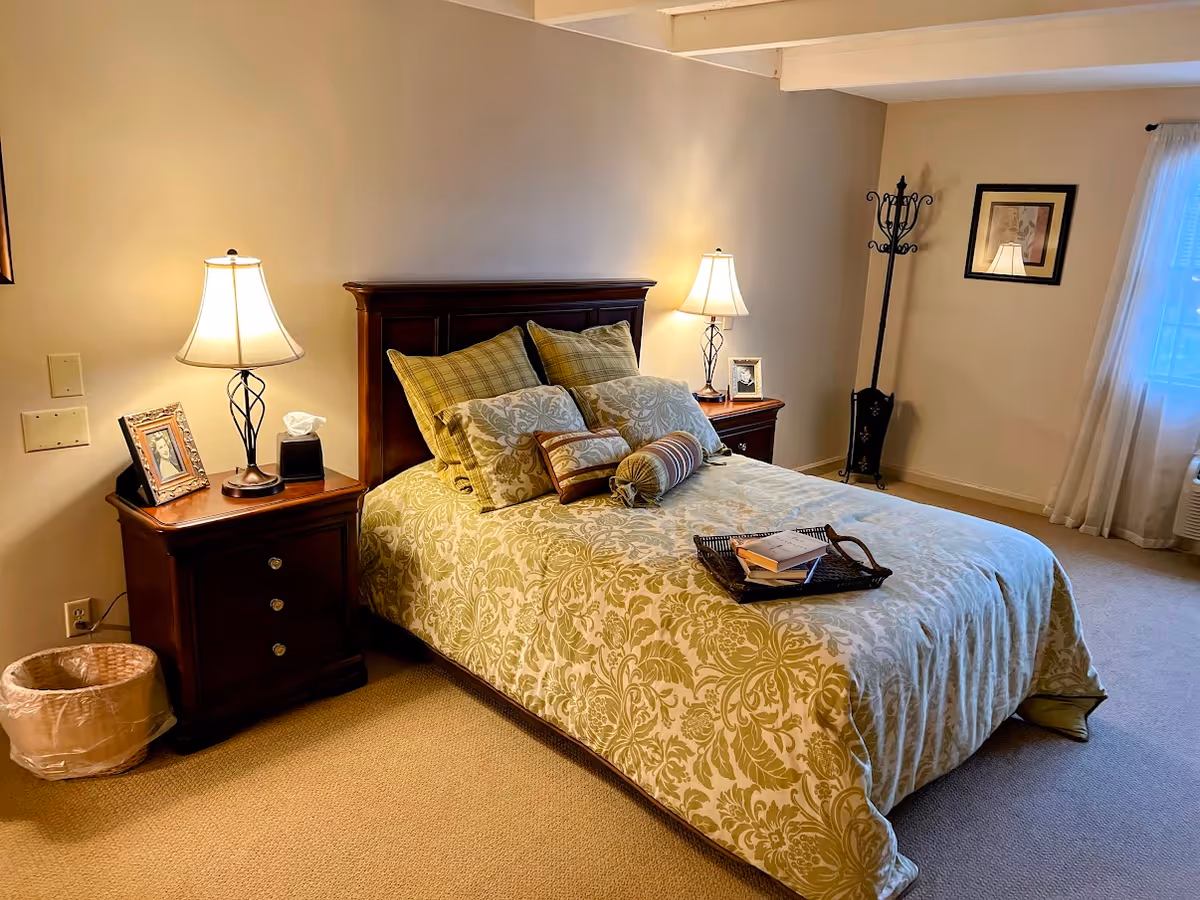 Neatly made bed with dark wood headboard, matching nightstands, lamps, and a sunlit windowed bedroom.