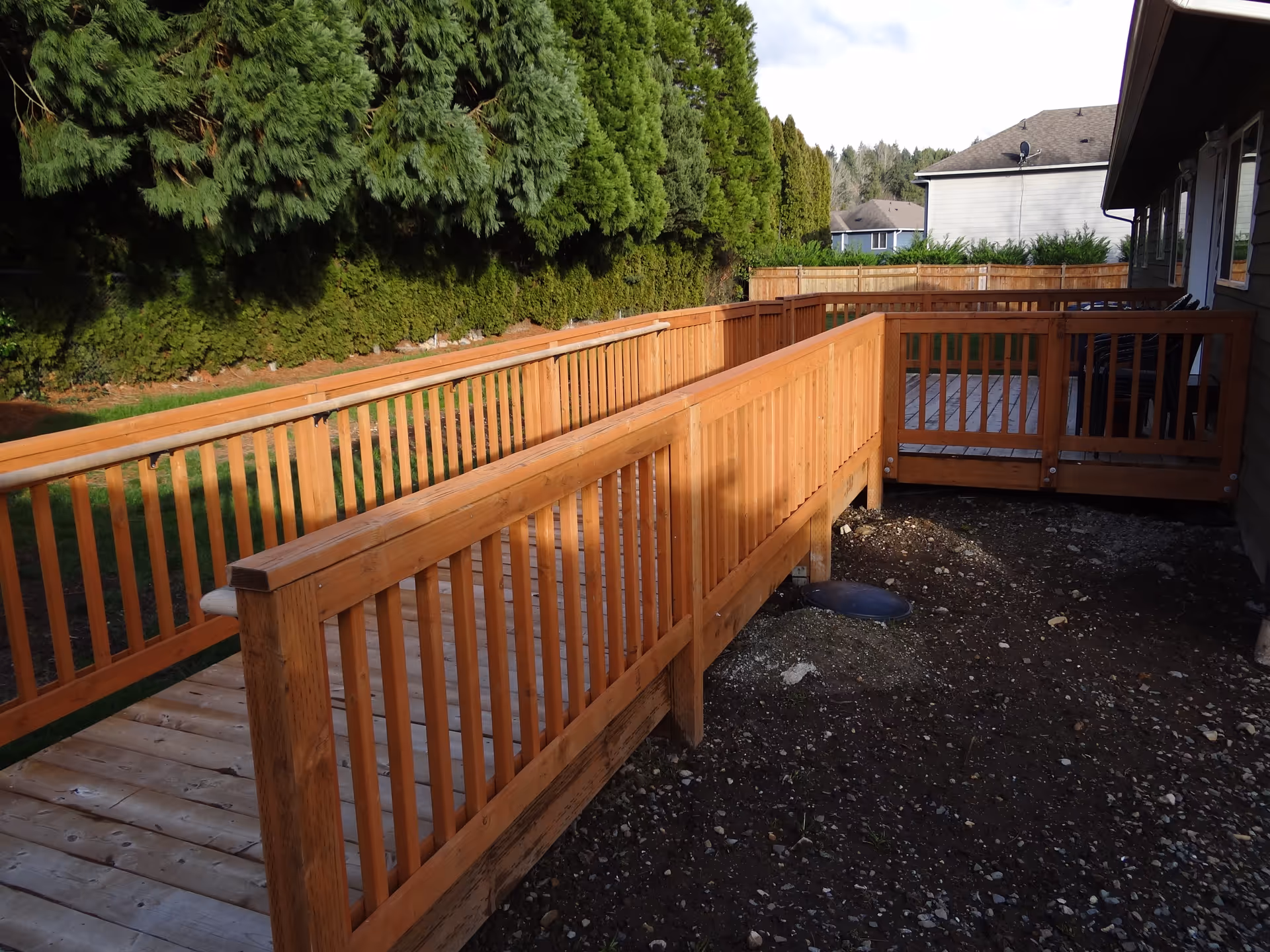 Wooden deck railing extends beside a house with evergreen trees behind.