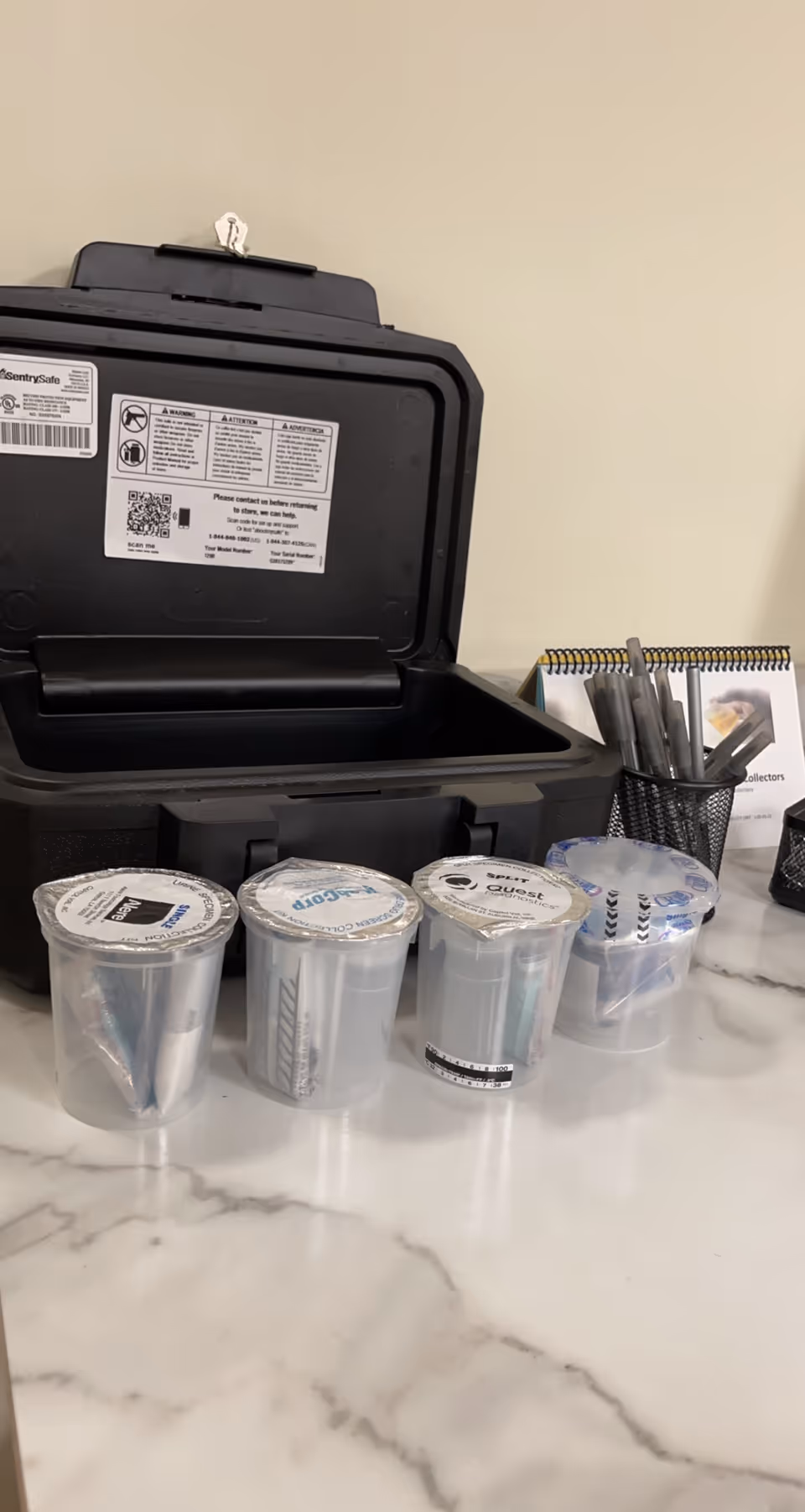 Countertop with a black, open-top device and several labeled plastic cups.