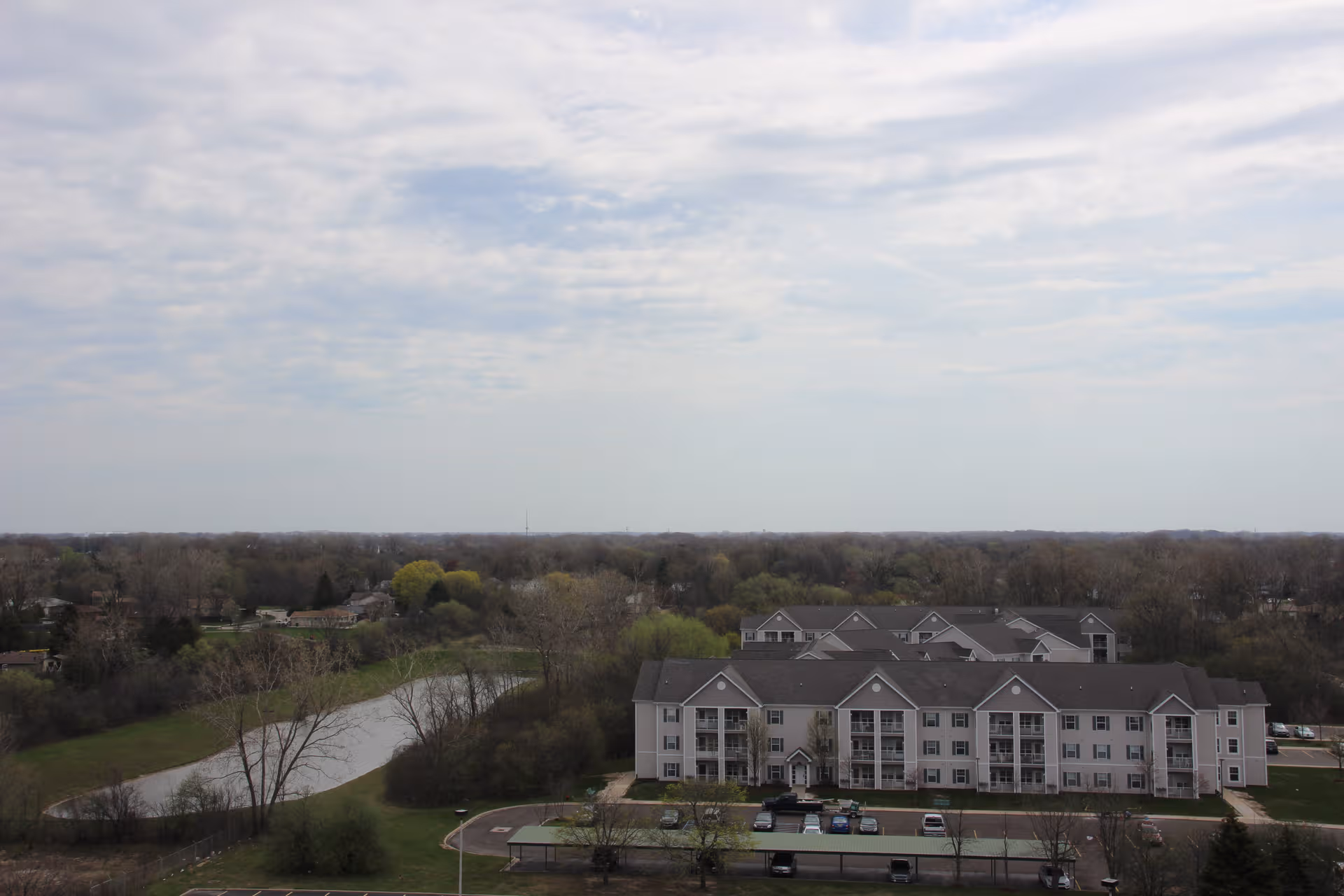 Exterior view of a multi-wing senior living building with a parking lot and surrounding trees.