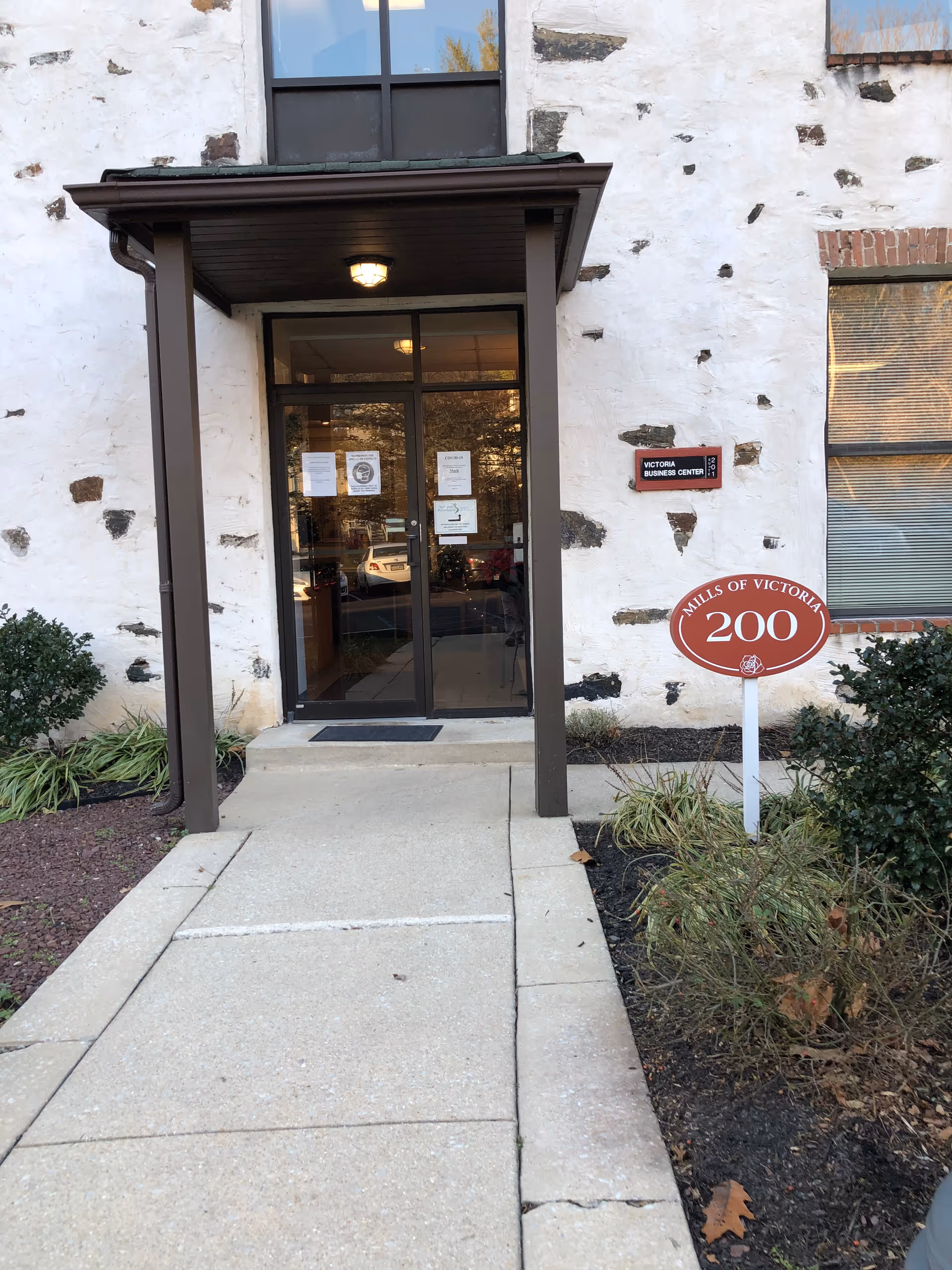 Exterior entrance with glass doors, a covered porch, and a concrete walkway.