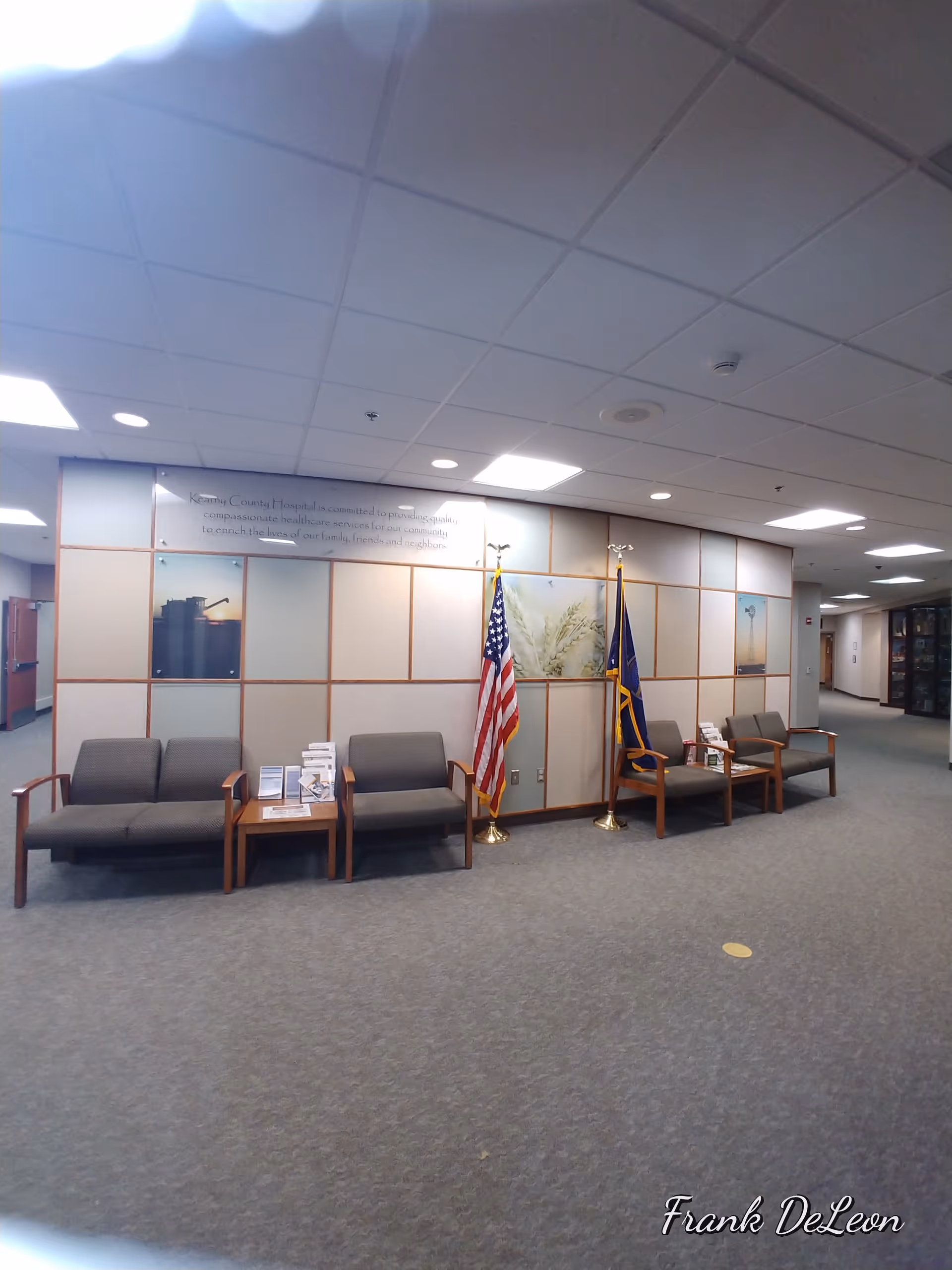 Hospital lobby with gray seating, tables, and flags near wall panels.