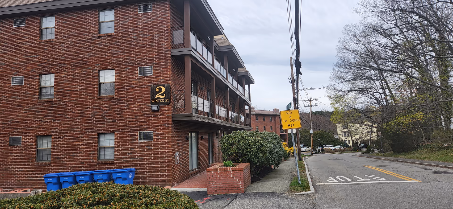 Brick senior living building with balconies along a street and a stop sign nearby.
