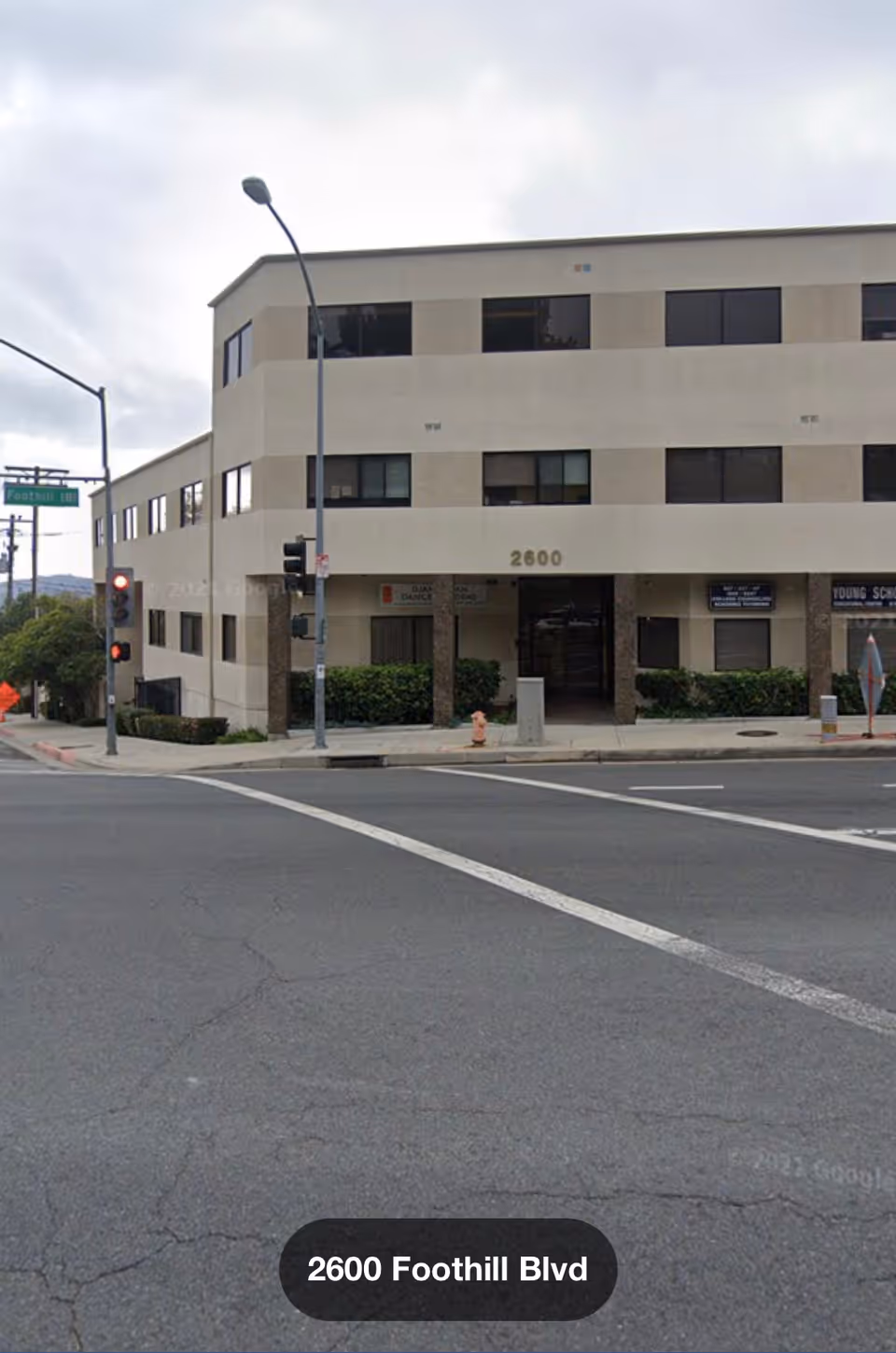 Three-story beige building on a city street with an entrance and signs nearby.