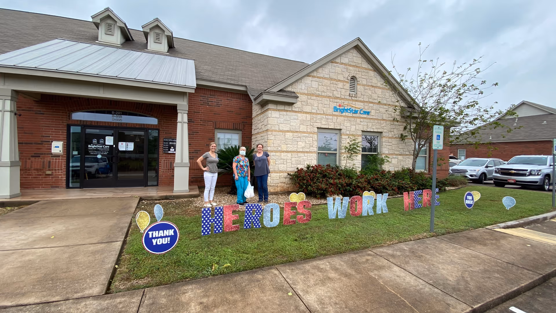 Exterior view of BrightStar Care Austin building with four people and 'Heroes Work Here' sign.