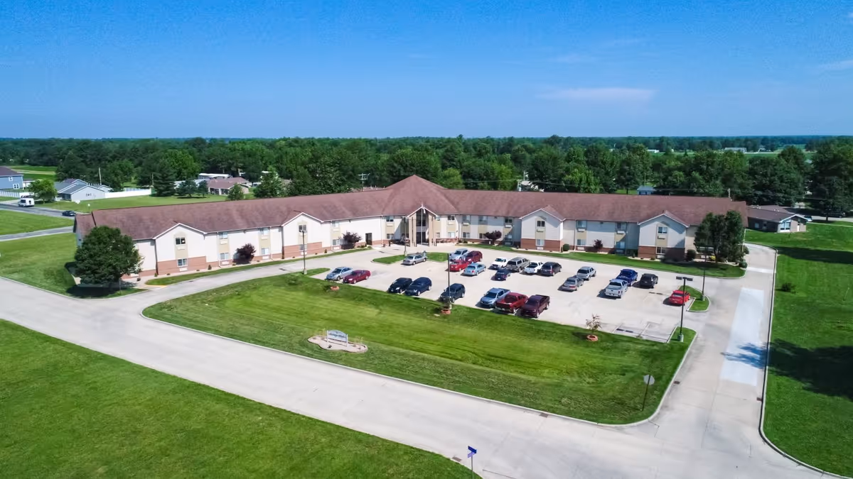 Aerial view of a single-story senior living facility with a central parking lot surrounded by lawns and trees.