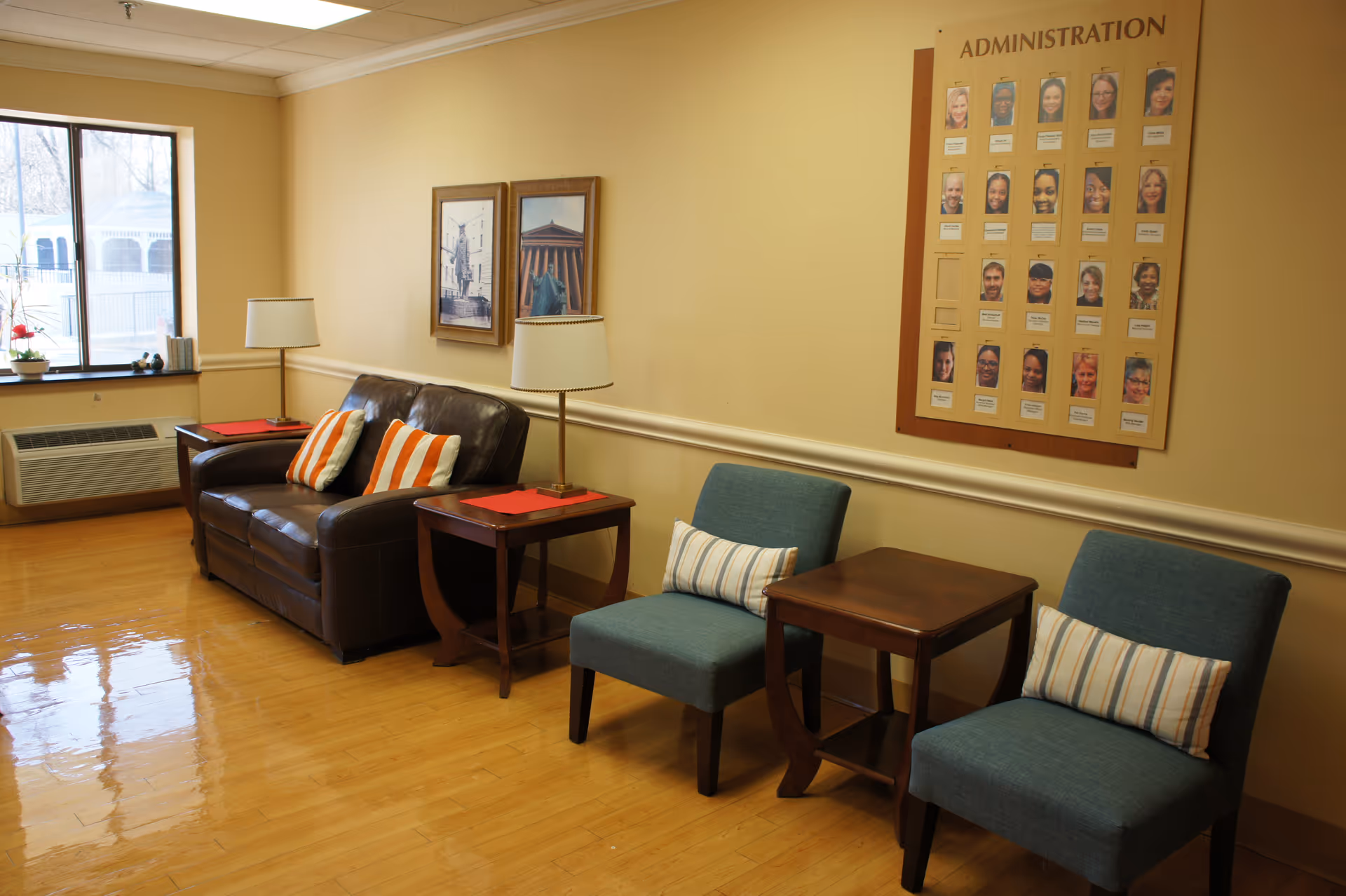 A cozy lounge area with leather sofa, blue chairs, side tables, and an administration board.