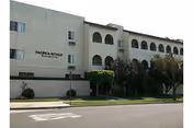 Exterior view of Pacifica Royale senior living facility with arched windows and greenery.