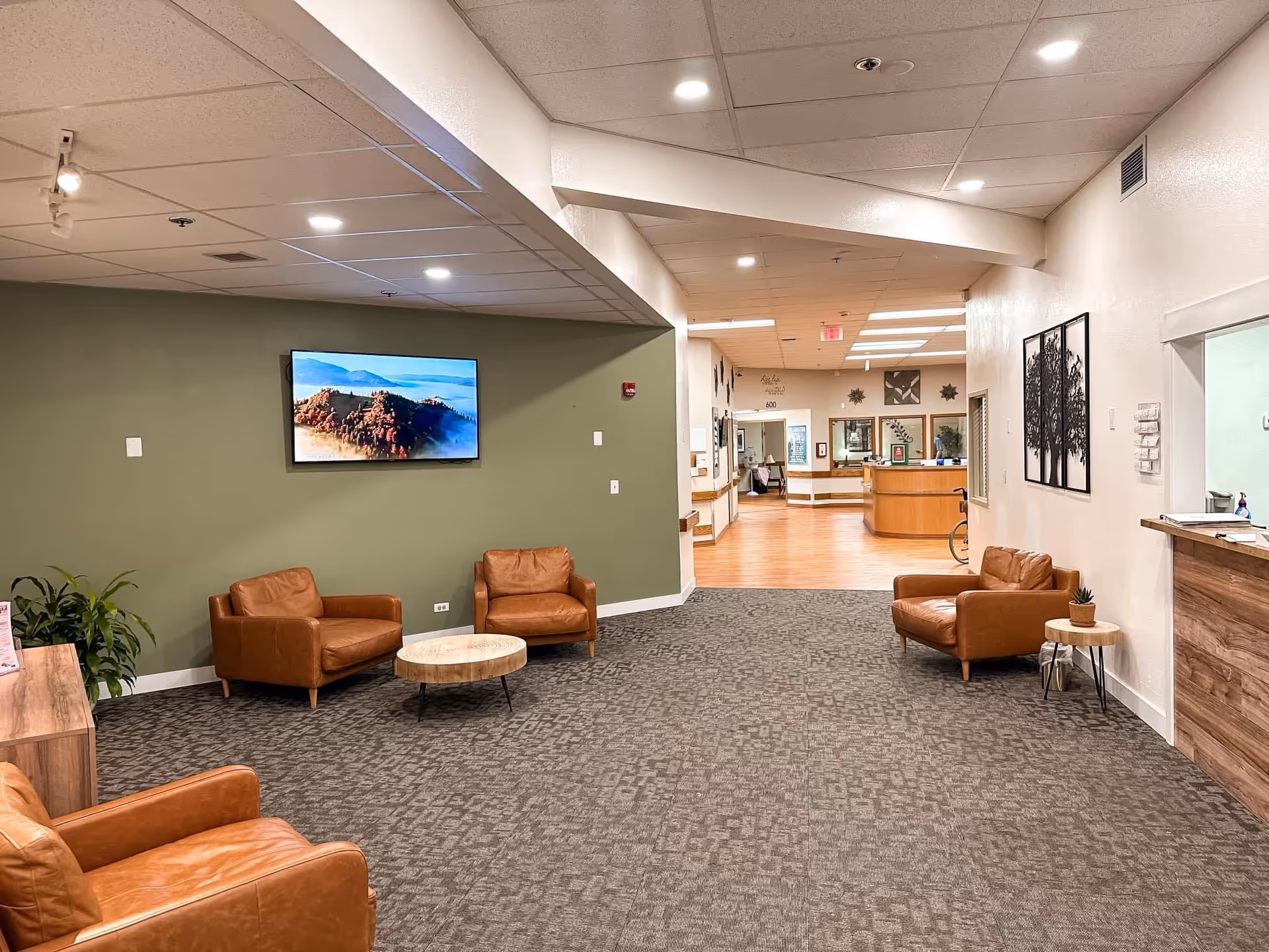 Modern senior living lobby with green accent wall, leather chairs, and a reception desk.