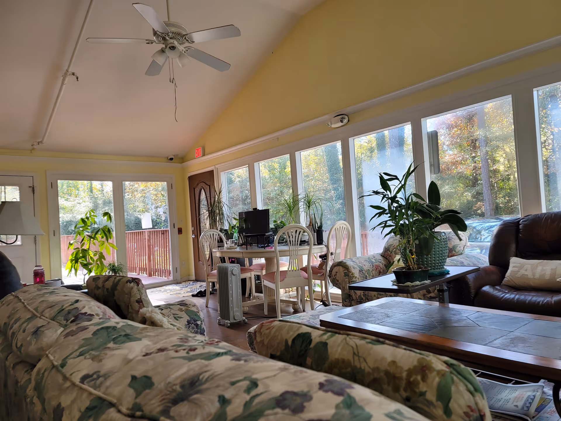 Bright lounge with floral sofas, large windows, plants, and a dining table.