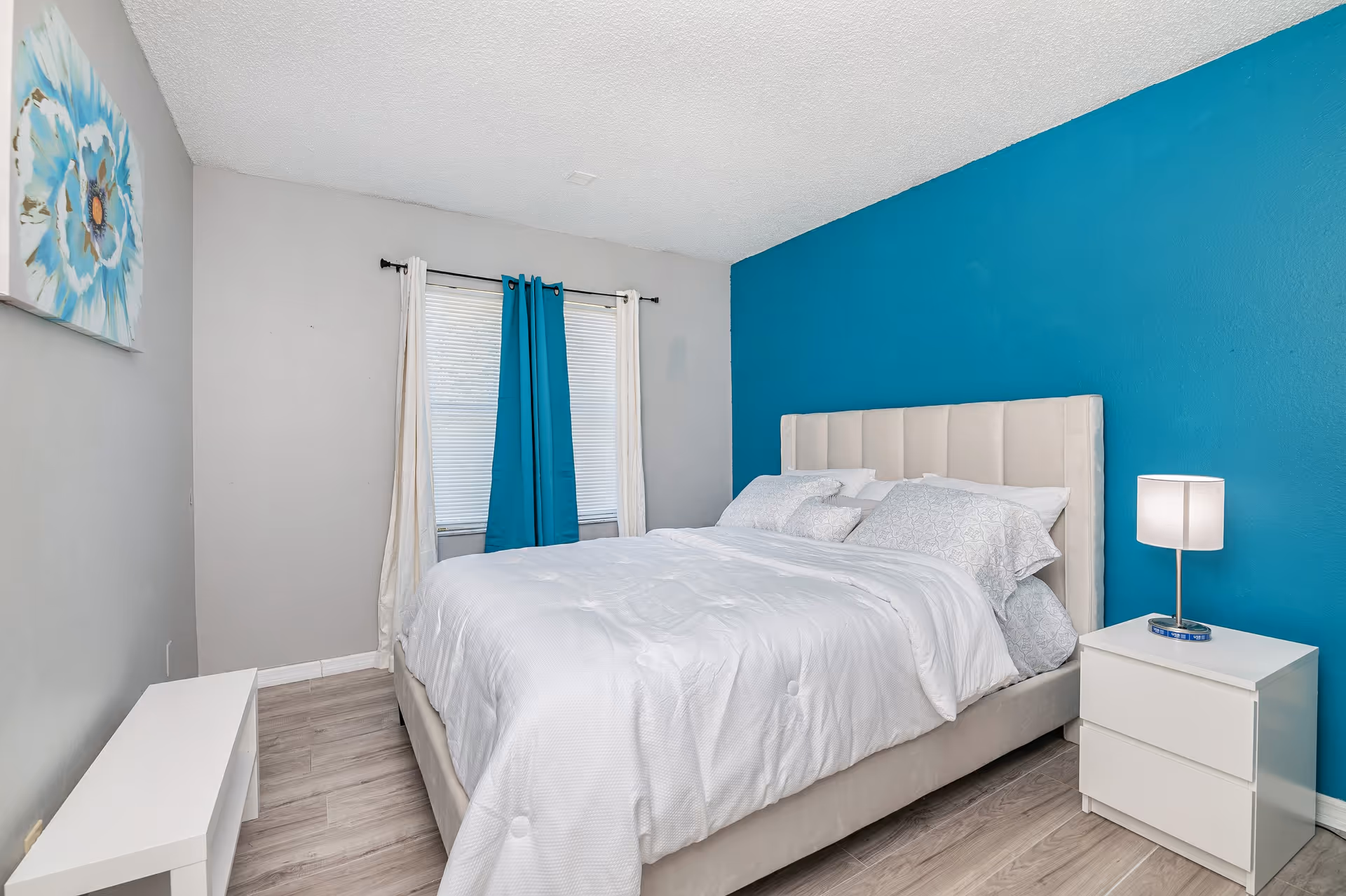Bright bedroom with white bedding, teal accent wall, and modern nightstand in a senior living room.