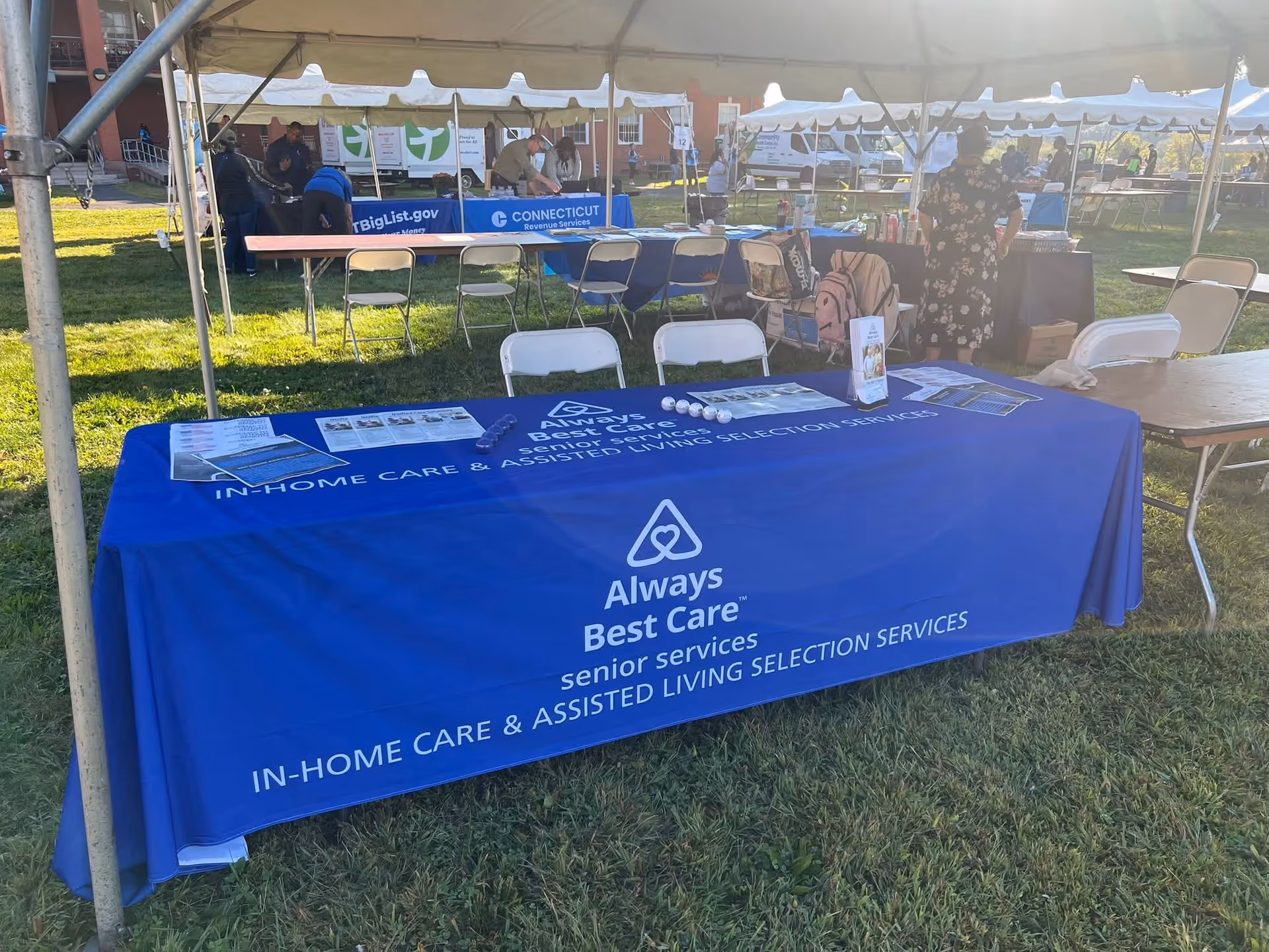 Outdoor event booth featuring a blue Always Best Care table under a tent.