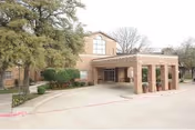 Exterior view of Cottonwood Creek Healthcare Community entrance with brick portico and surrounding landscaping.