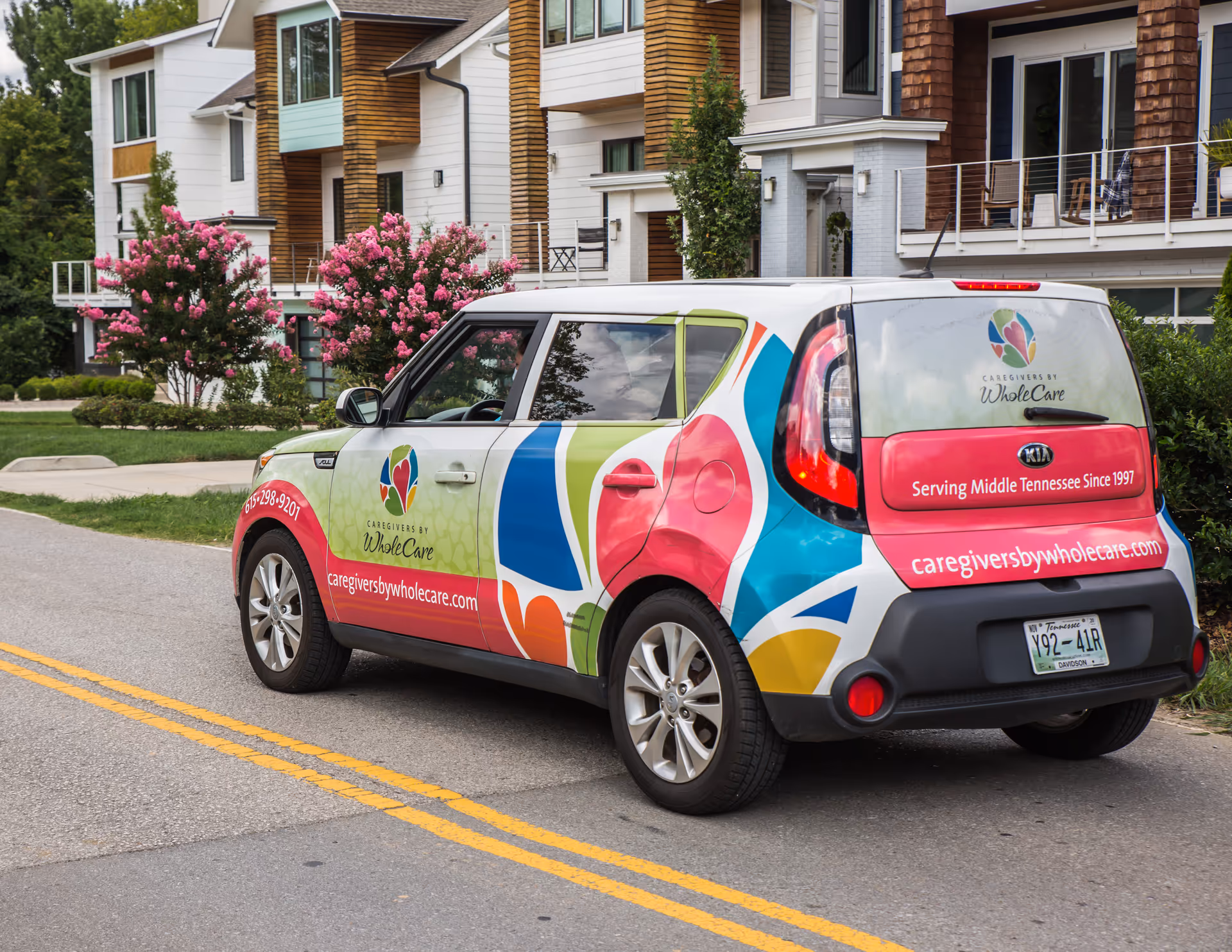 Colorful Caregivers by WholeCare van parked outside a modern senior living building.