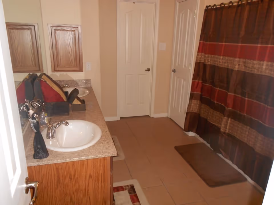 Interior bathroom with a double-sink vanity, mirror, and a shower with a brown striped curtain.