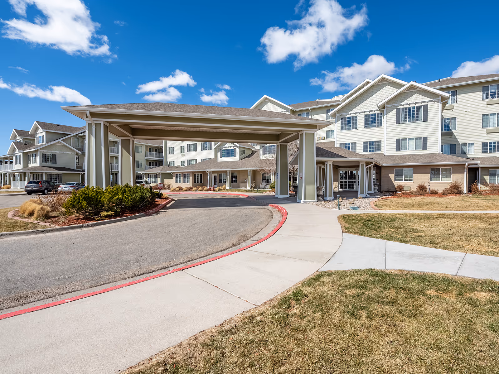 Wide view of Whispering Chase senior living facility exterior with a covered driveway and entrance.