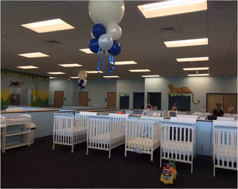 A room with multiple white cribs, balloons, and a front desk area.
