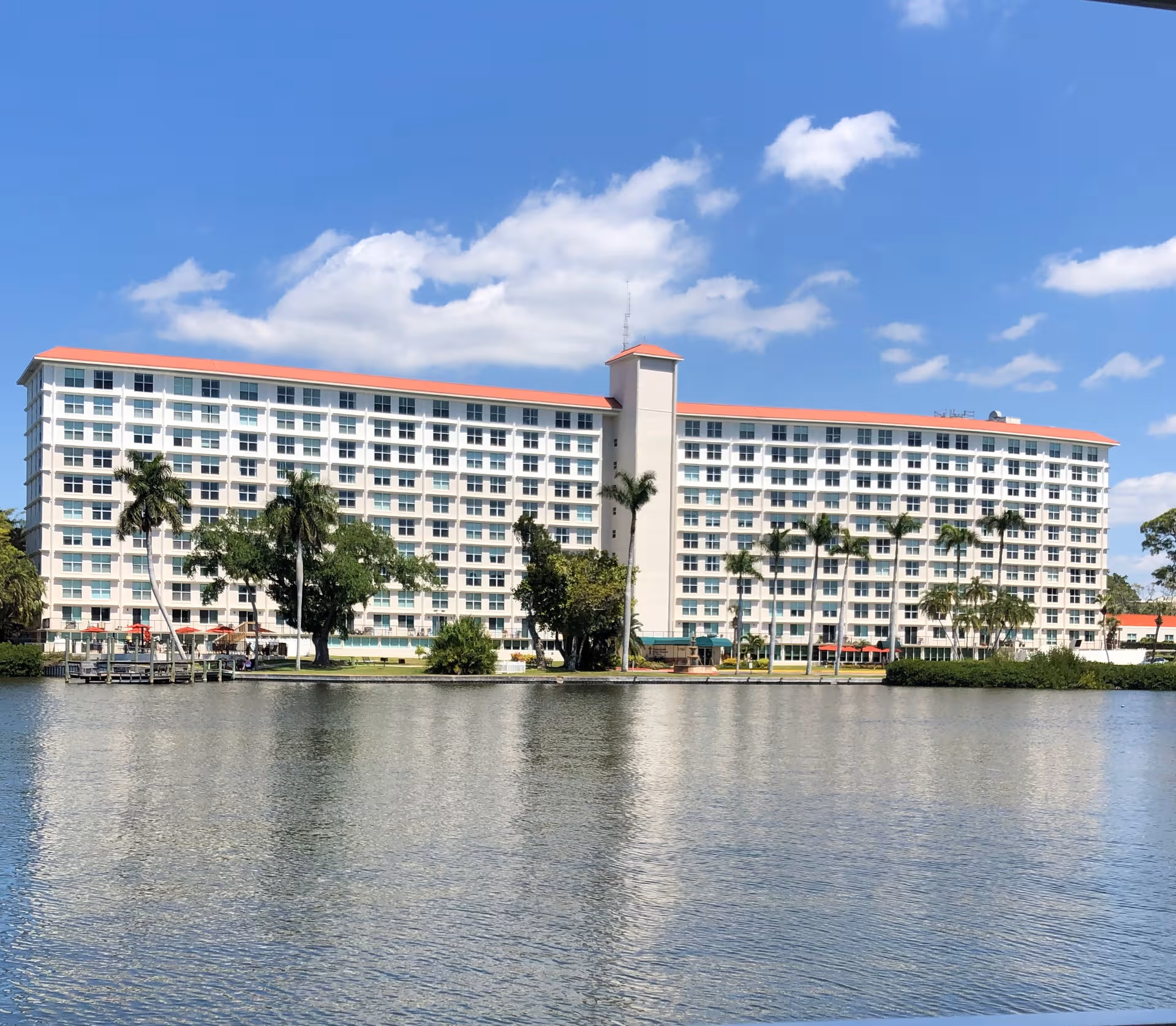 A large multi-story senior living building along the water with palm trees.