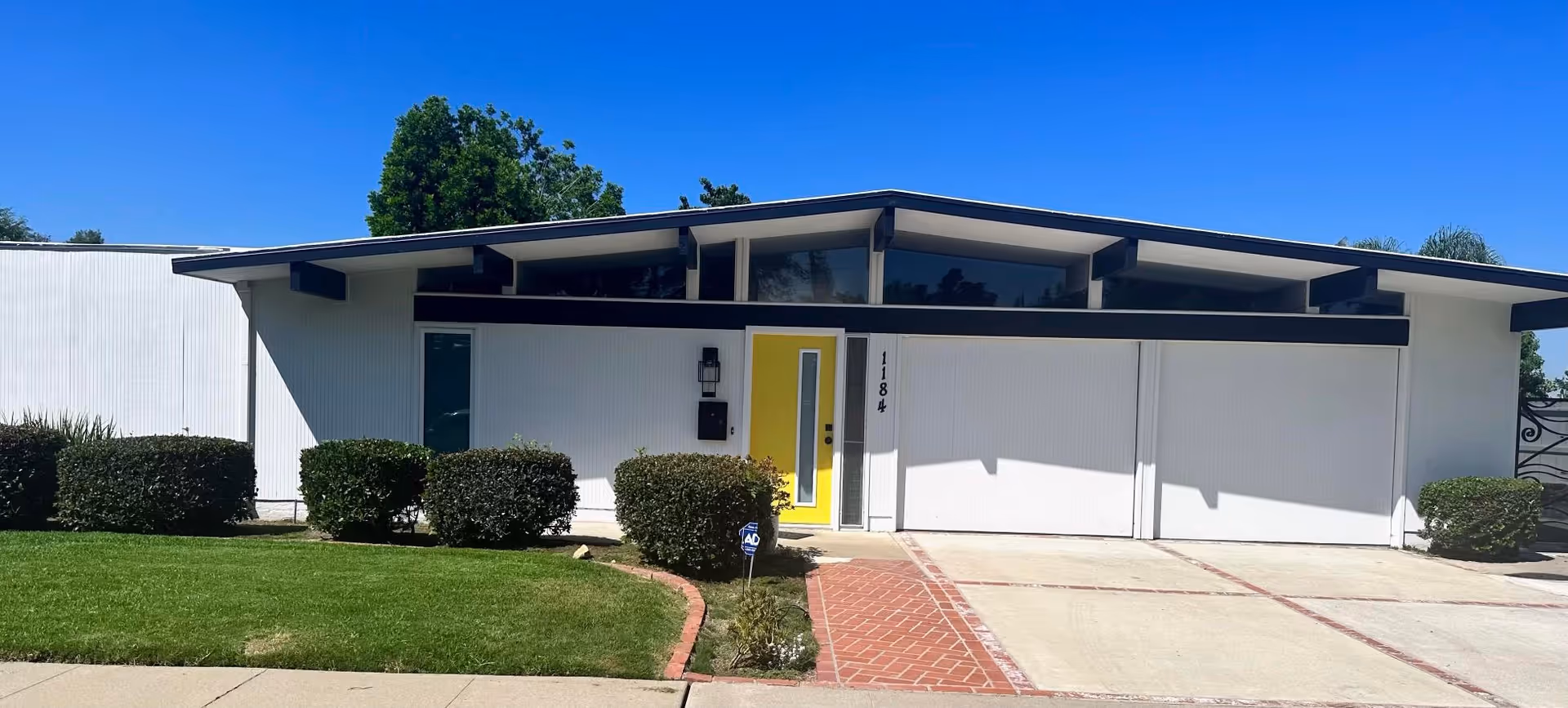 Modern single story senior care facility exterior featuring a yellow front door and trimmed shrubs.
