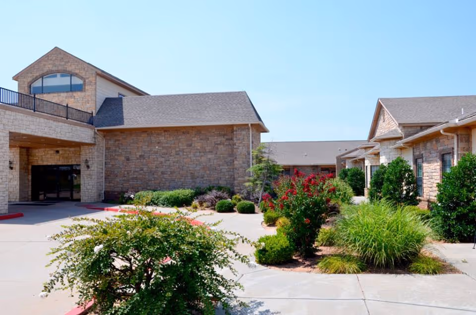 Stone retirement village exterior with landscaped entrance and clear blue sky.