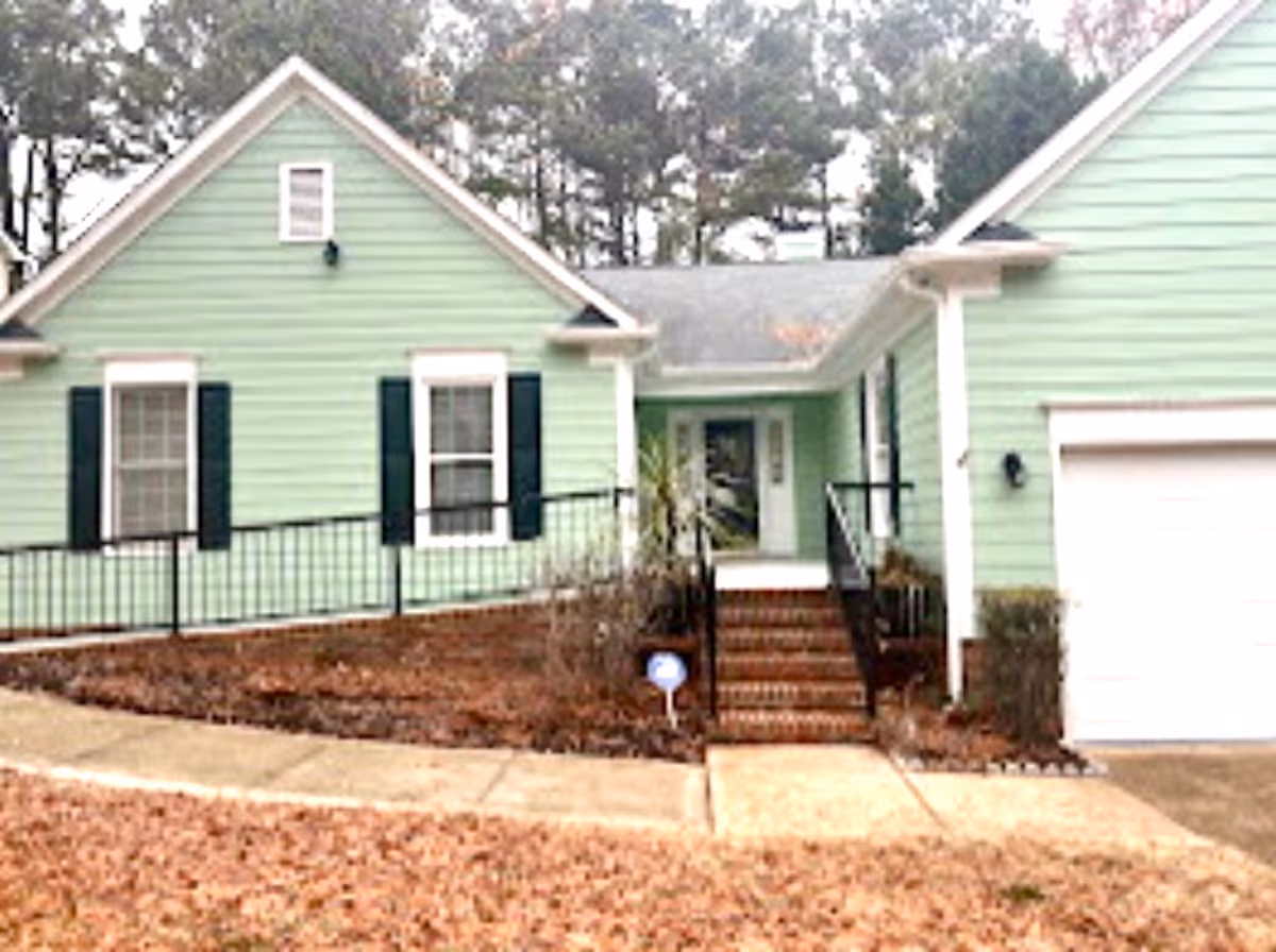 Mint-green senior facility exterior with entry stairs, railing, and a garage door.