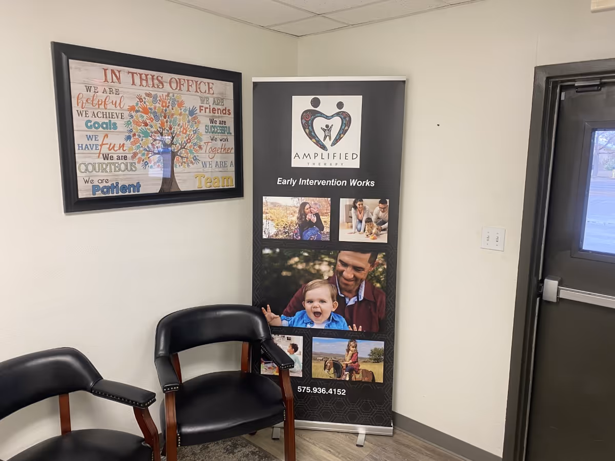 Interior office waiting area with black chairs, an Amplified Therapy banner, and framed wall art.