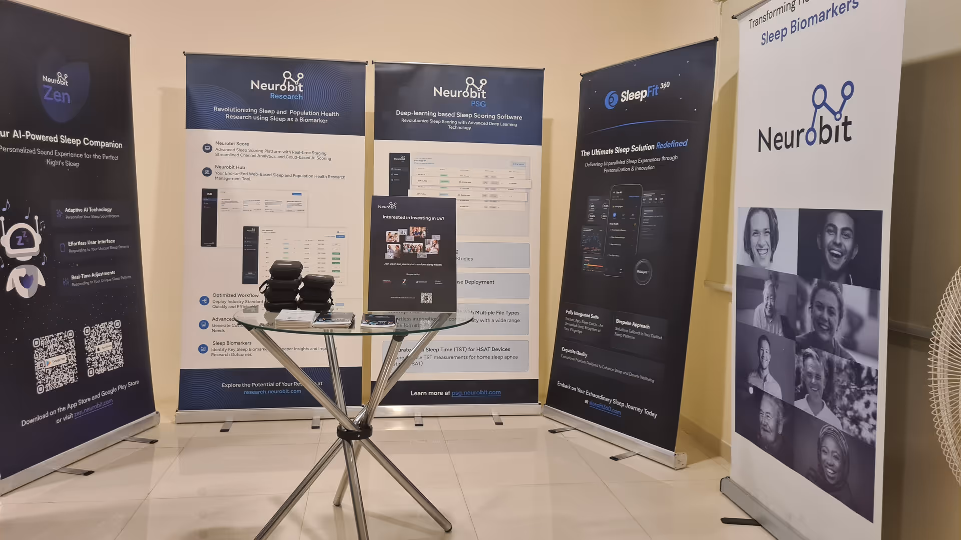 Indoor exhibition area with multiple Neurobit banners and a glass table.
