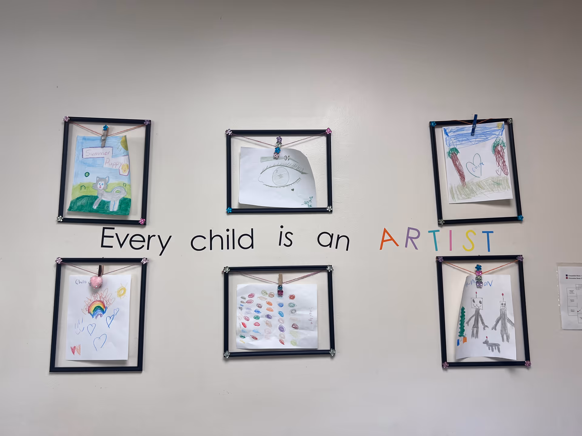Wall displays children's framed drawings with the phrase Every child is an ARTIST.
