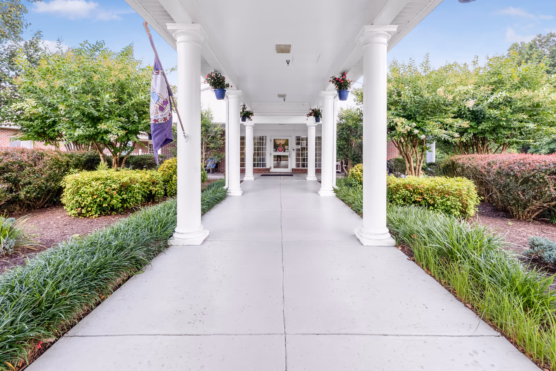 Covered walkway with white columns leads to the Meadows Nursing Center entrance amid shrubs.
