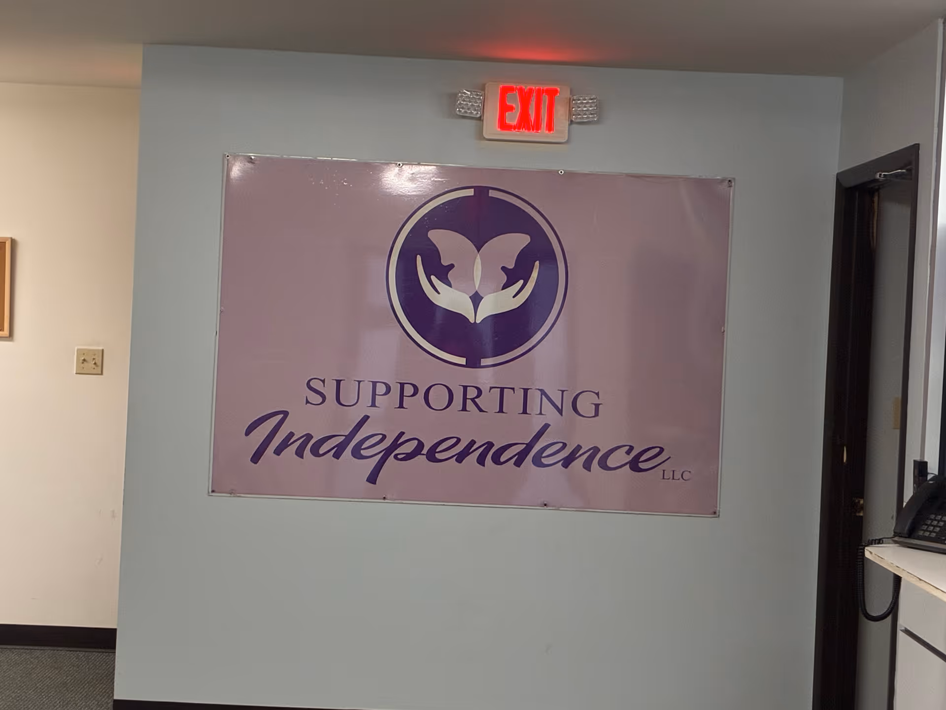 Inside a facility hallway, a large lavender banner reads Supporting Independence LLC on the wall.