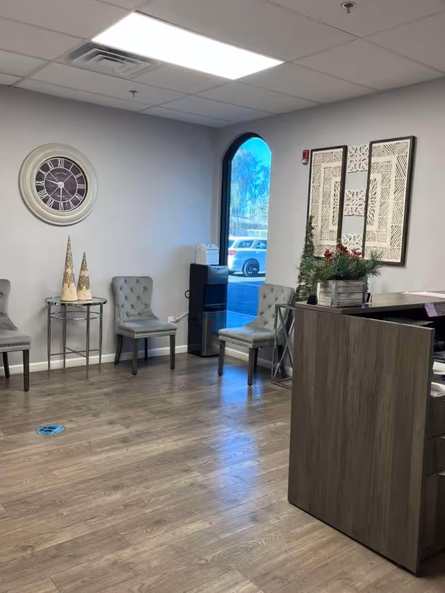 Reception area with chairs along the wall, clock, arched window, and front desk.