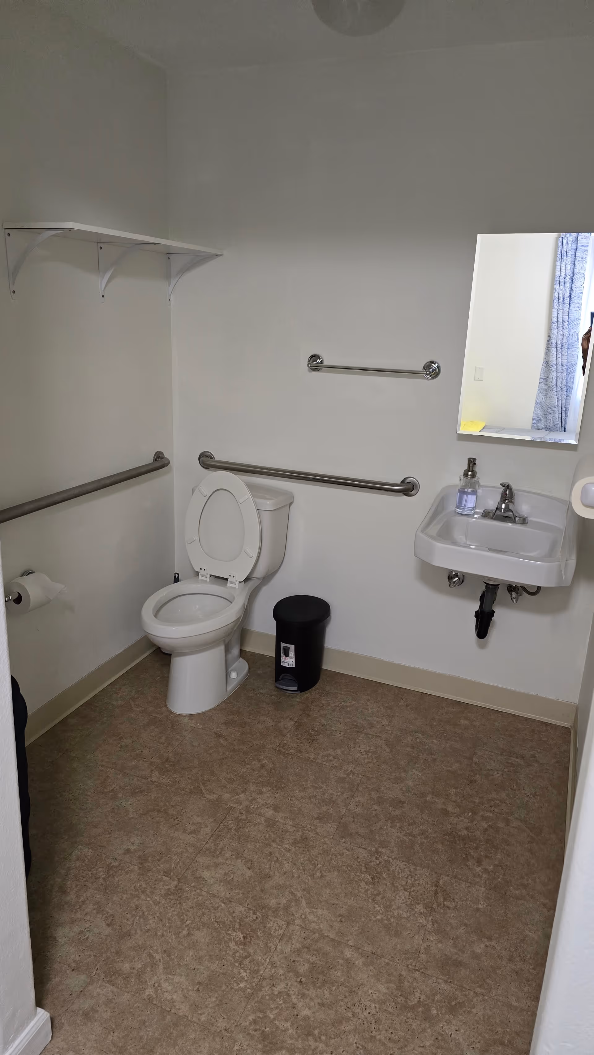 Accessible bathroom with toilet, sink, and several grab bars in a senior care home.