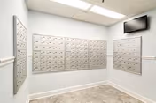 Small mailroom with rows of mailboxes along pale blue walls and a wall-mounted screen.