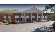 Two-story brick senior living building with a white columned entrance and a driveway.