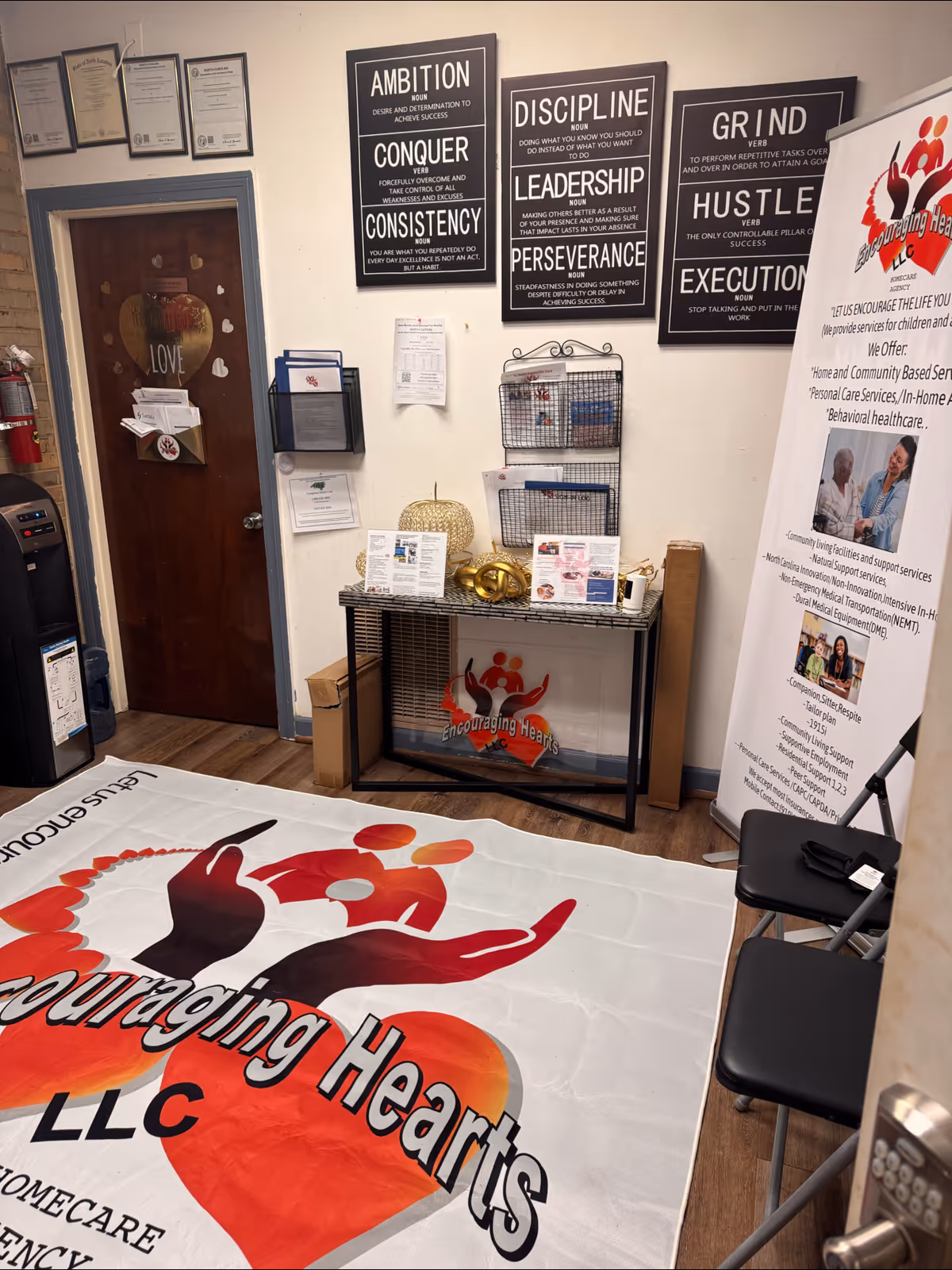 Interior lobby area with a desk, motivational posters, a logo rug, and Encouraging Hearts LLC banner.