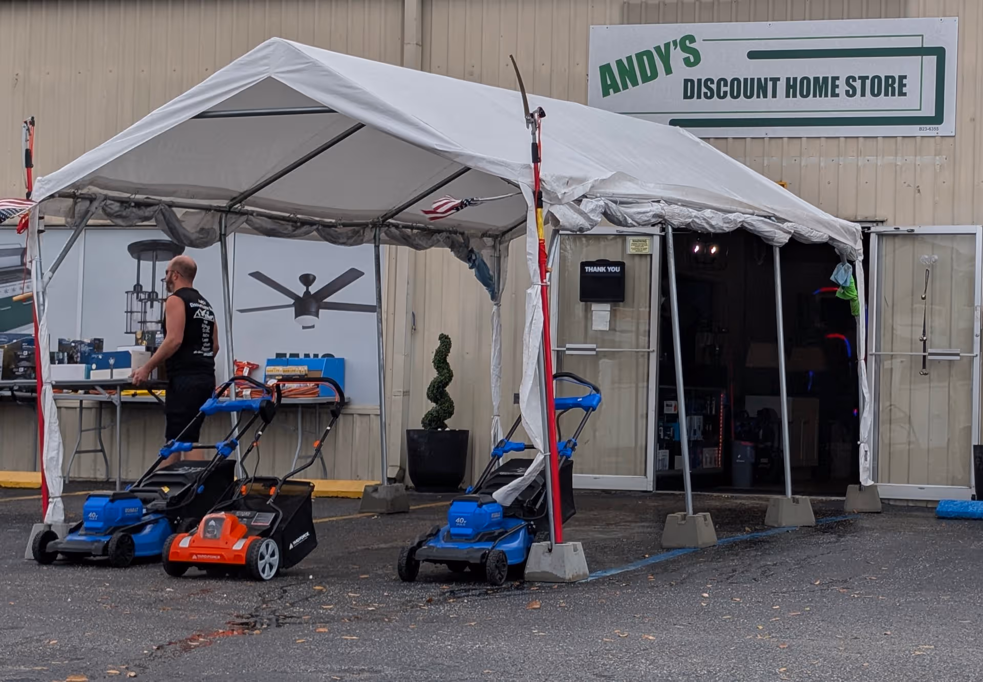 Exterior storefront with a white tent and lawnmowers outside Andy's Discount Home Store