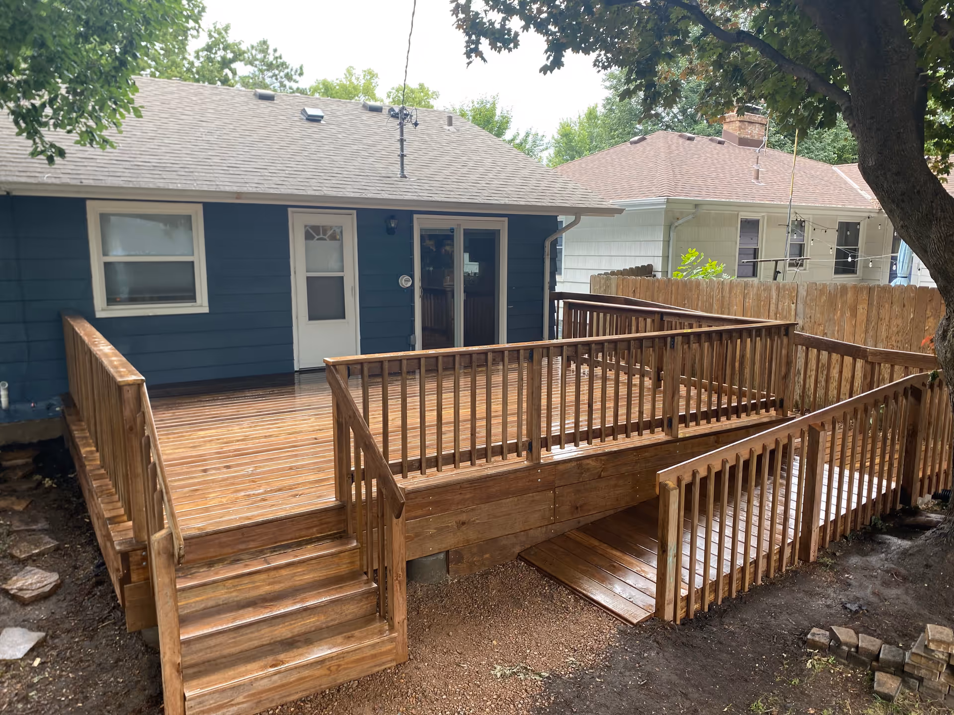 Blue single-story house with a large wooden deck and stairs outdoors.