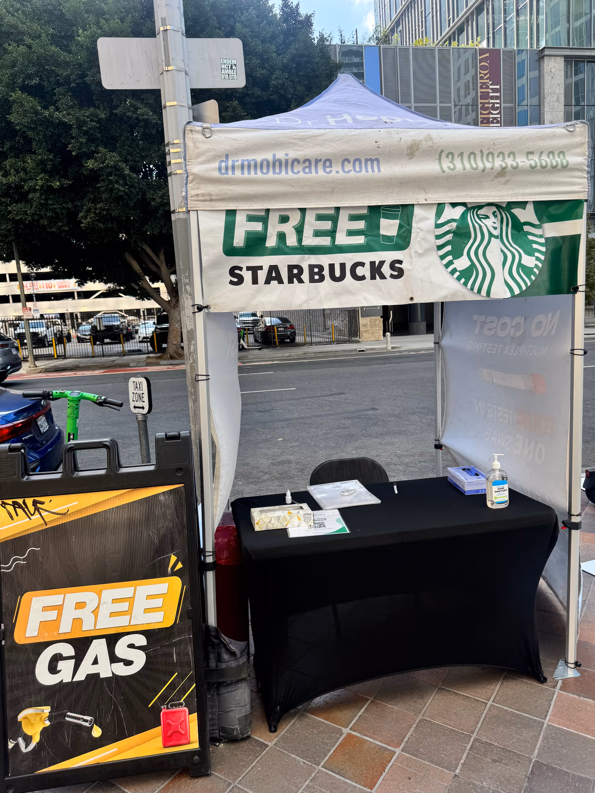 Outdoor promotional tent on sidewalk with a table and free Starbucks and free gas banners.