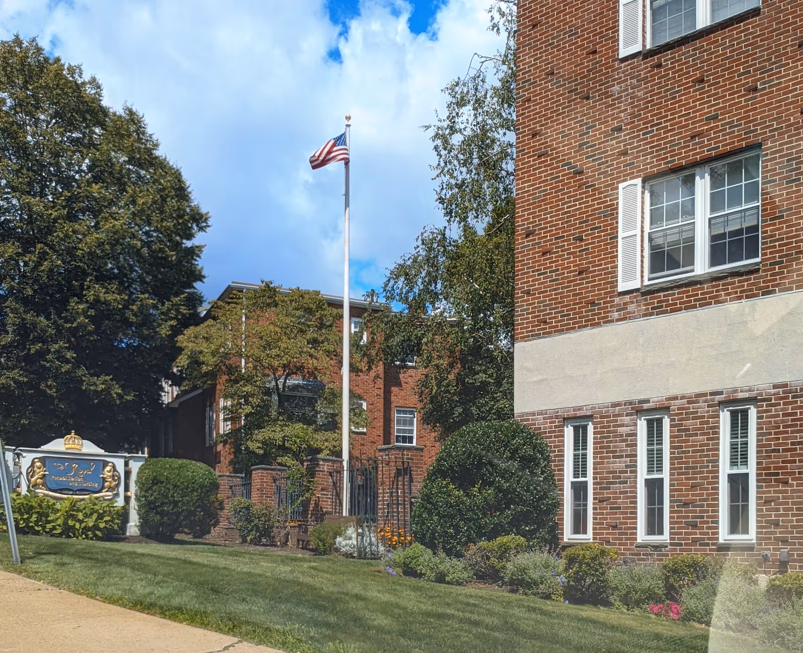 Brick senior living building with flagpole, manicured lawn, and shrubs in front