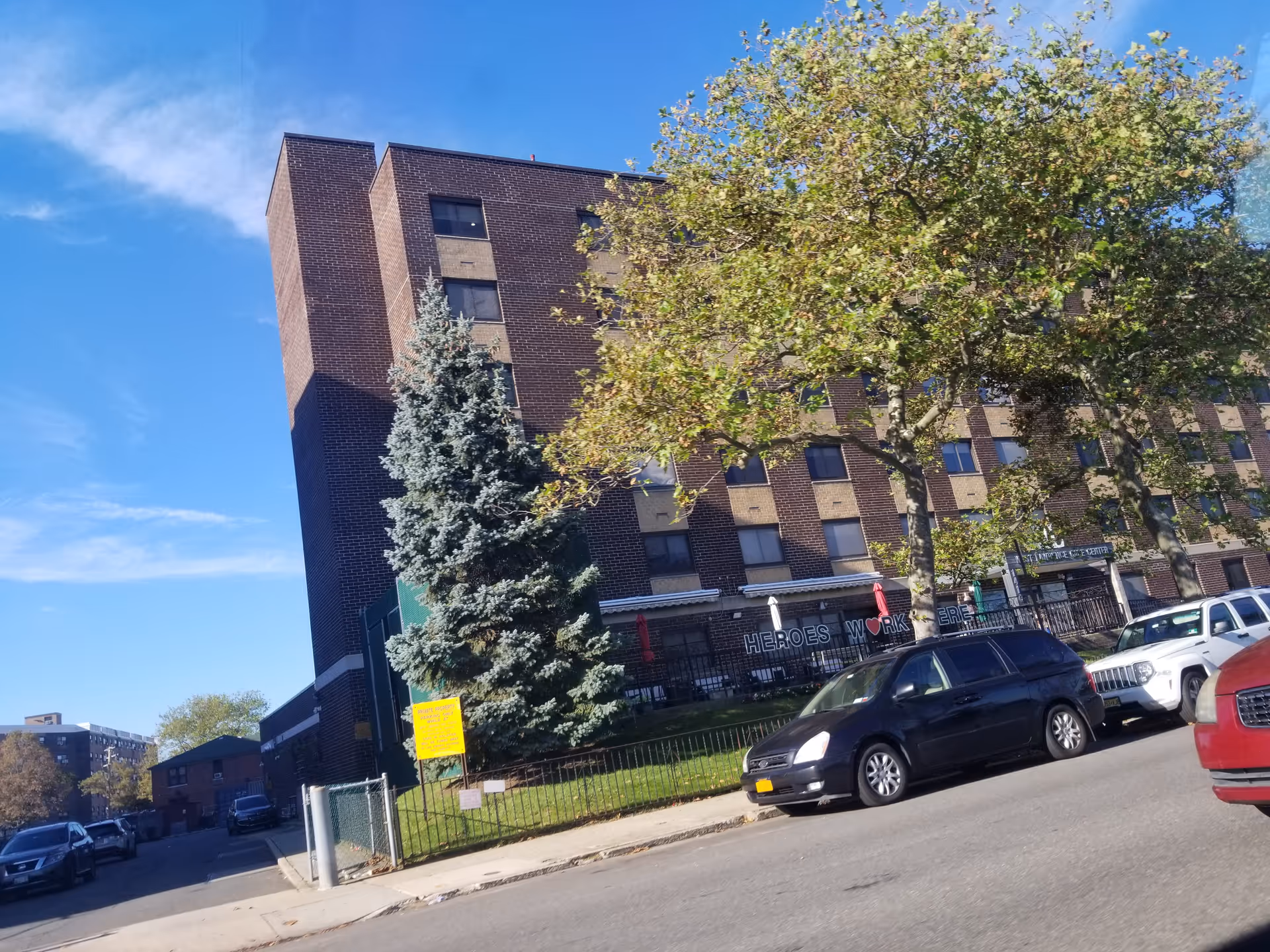 Front exterior of West Lawrence Care Center with brick building, trees, and parked cars.