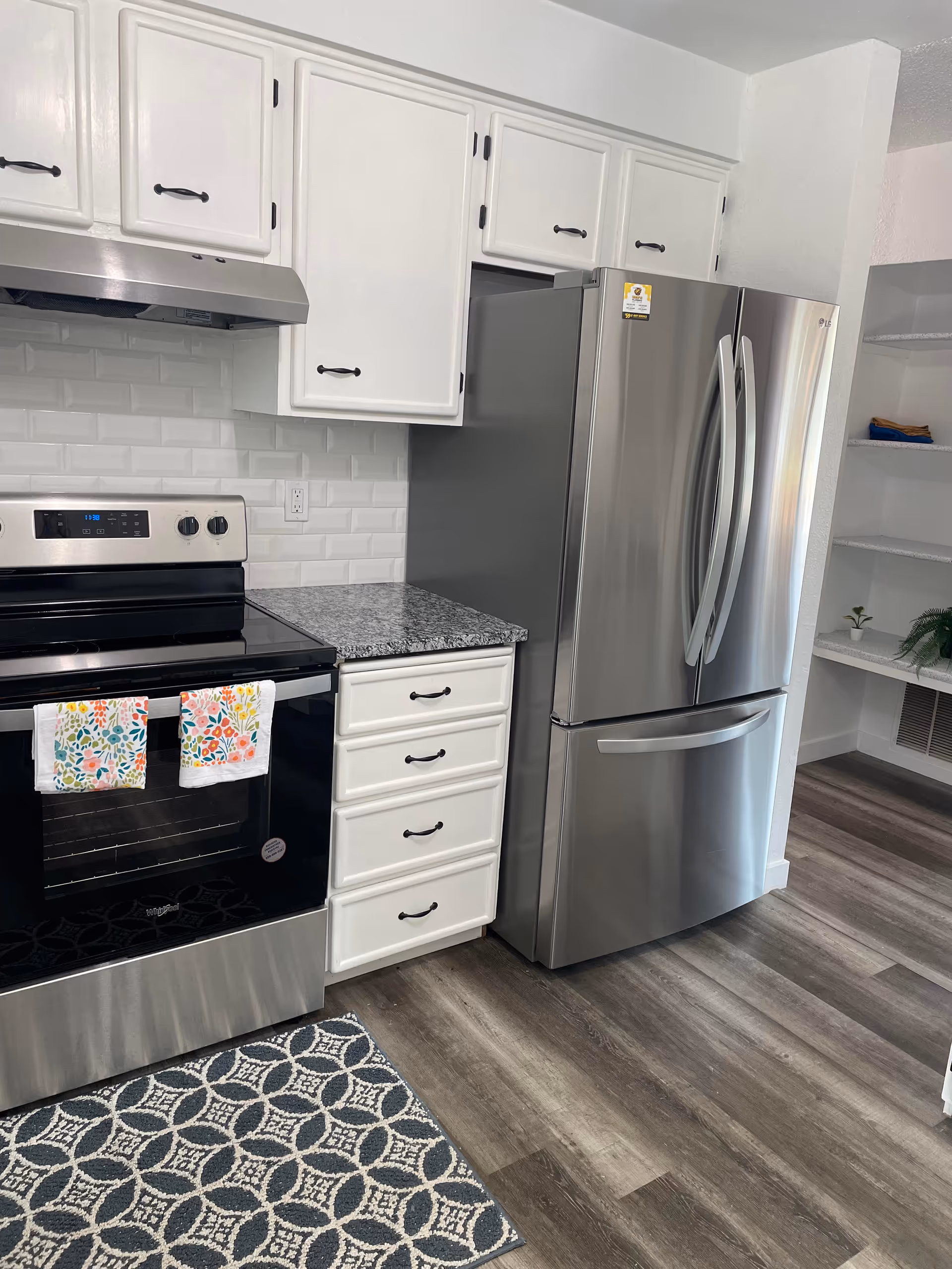 Modern kitchen with stainless steel appliances, white cabinets, granite counters, and a decorative rug.