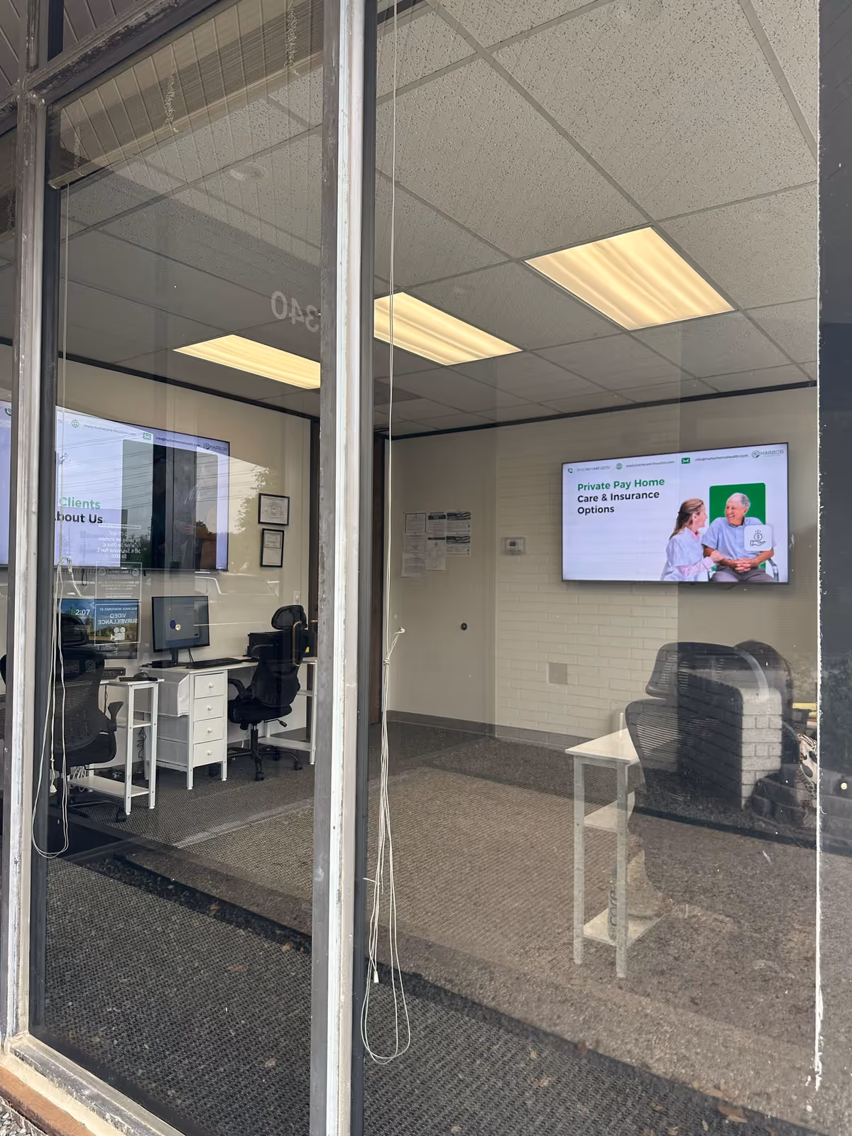 Office reception area of Harbor Home Care with desks, chairs, and a wall-mounted screen.