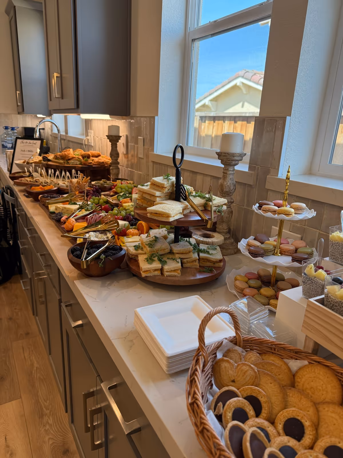 Buffet-style spread of sandwiches, pastries, and snacks along a long marble kitchen island.