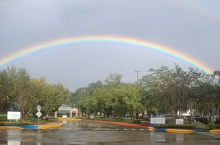 Outdoor parking lot with a double rainbow over trees near a senior living facility.