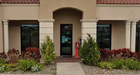 A senior living facility entrance with archway, columns, and landscaped shrubs.