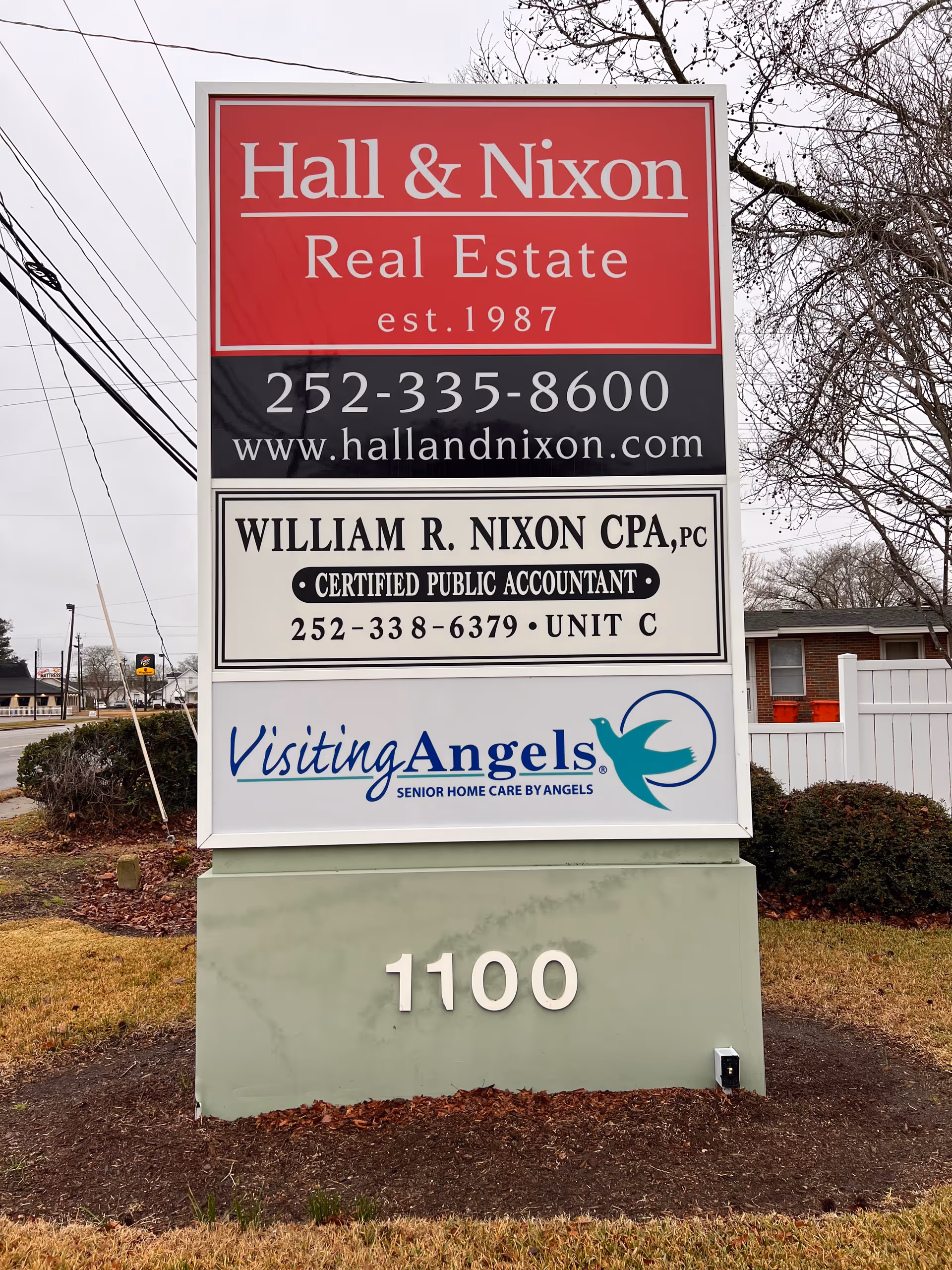 Outdoor multi-sign display with Visiting Angels logo beside real estate and CPA ads.